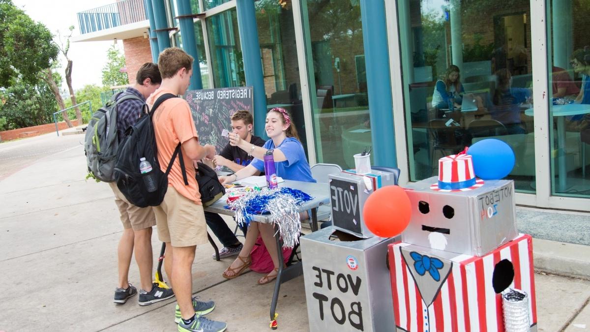 Students at table outside talking to other standing students