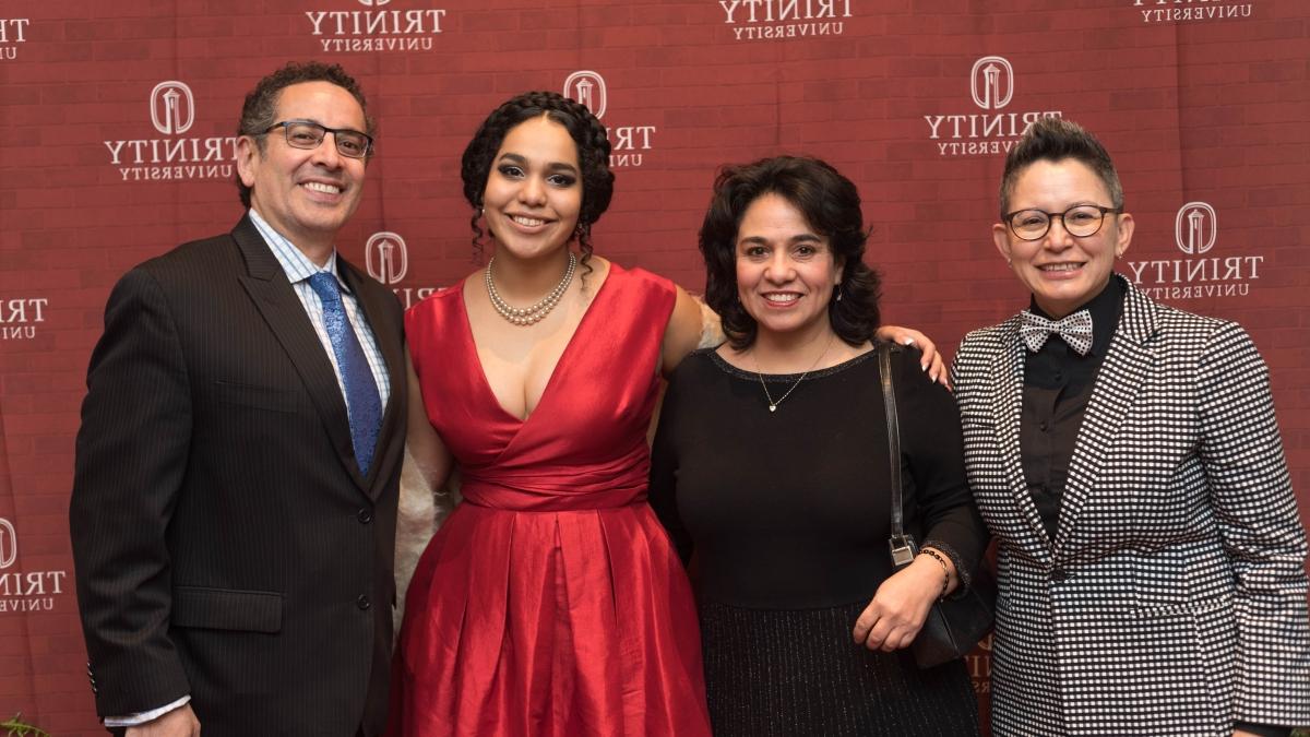 four Trinity donors stand in front of a logo background